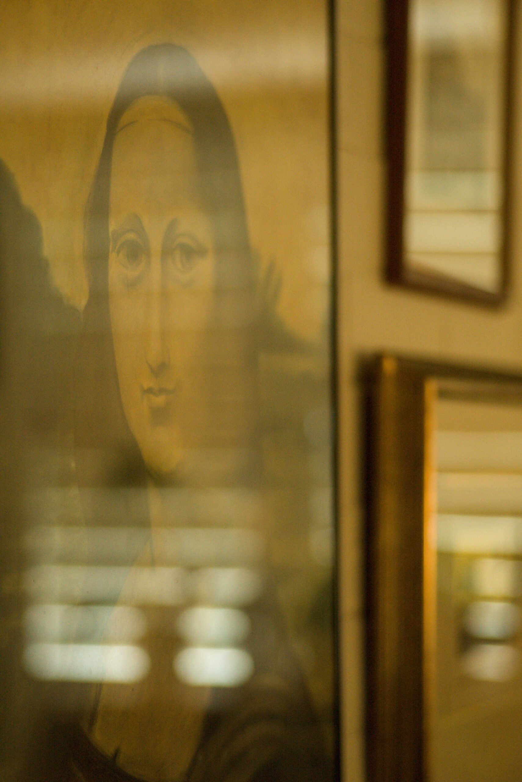 Beauty Everyday, 20: Detail of a framed artwork with window reflections in the glass, in a softly lit interior.