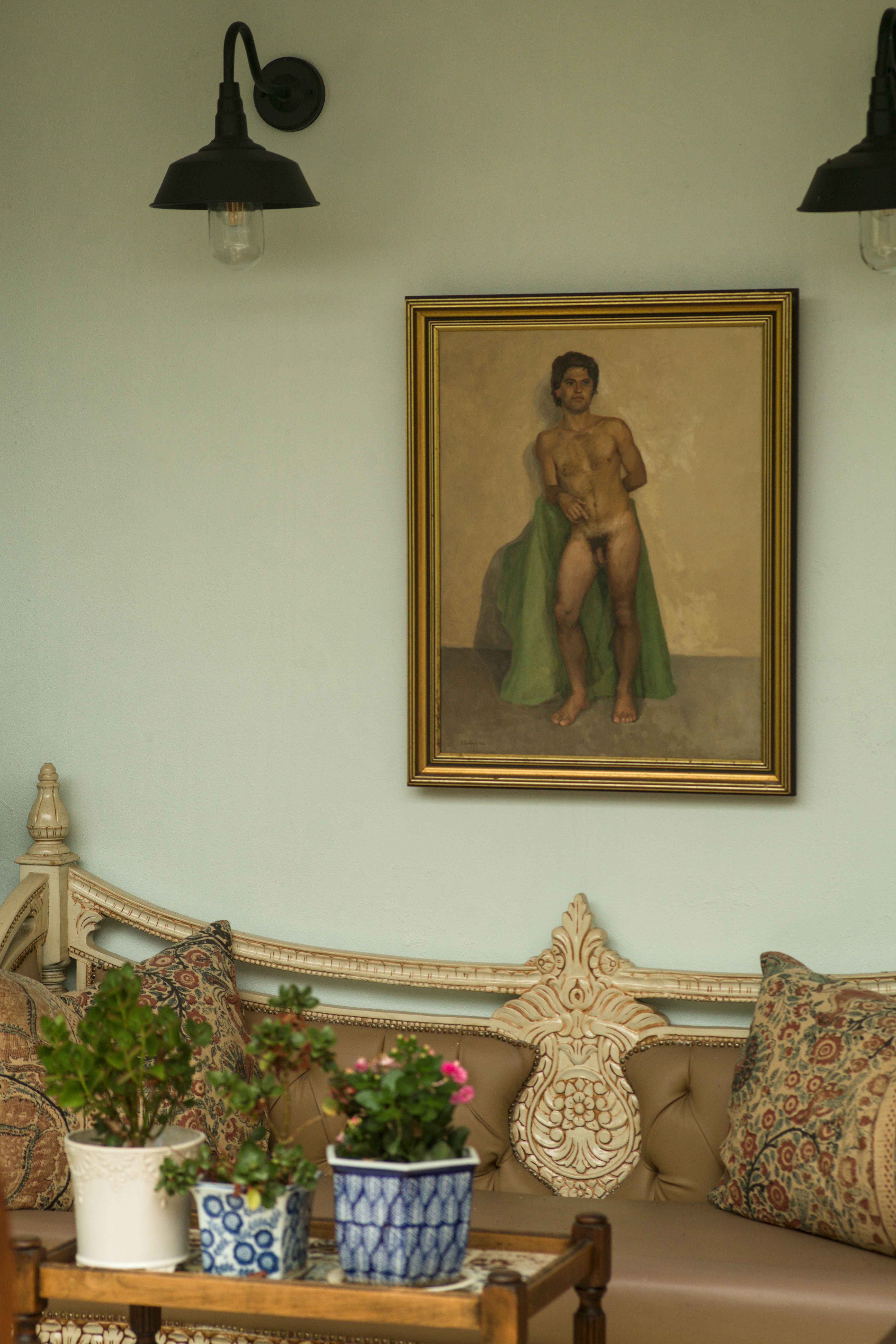 Beauty Everyday, 4: Framed male nude painting in soft daylight above a leather sofa and wooden trolley with three potted plants.