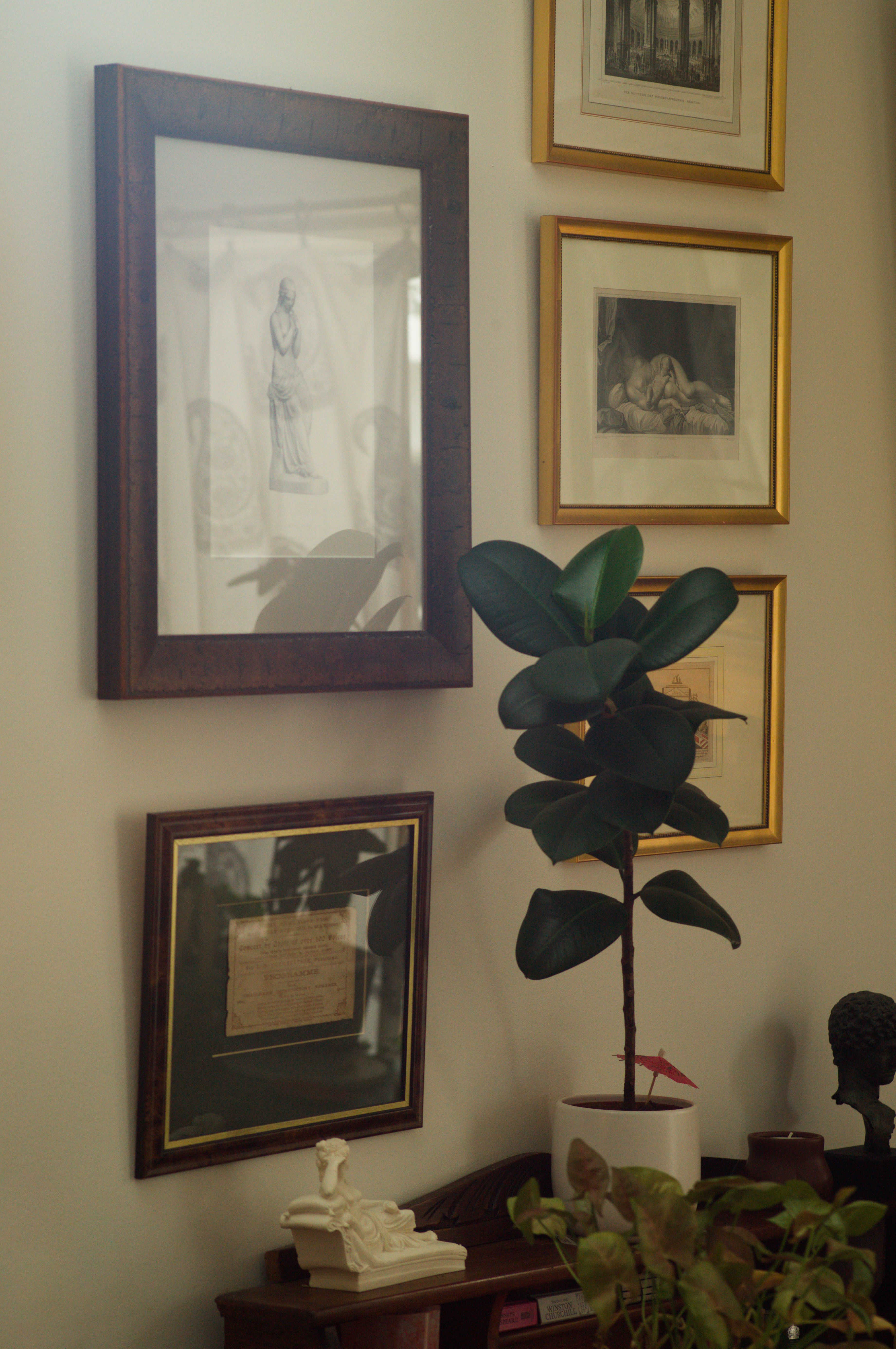 Beauty Everyday, 8: Cluster of framed artworks arranged above a low table with everyday objects in a domestic interior.