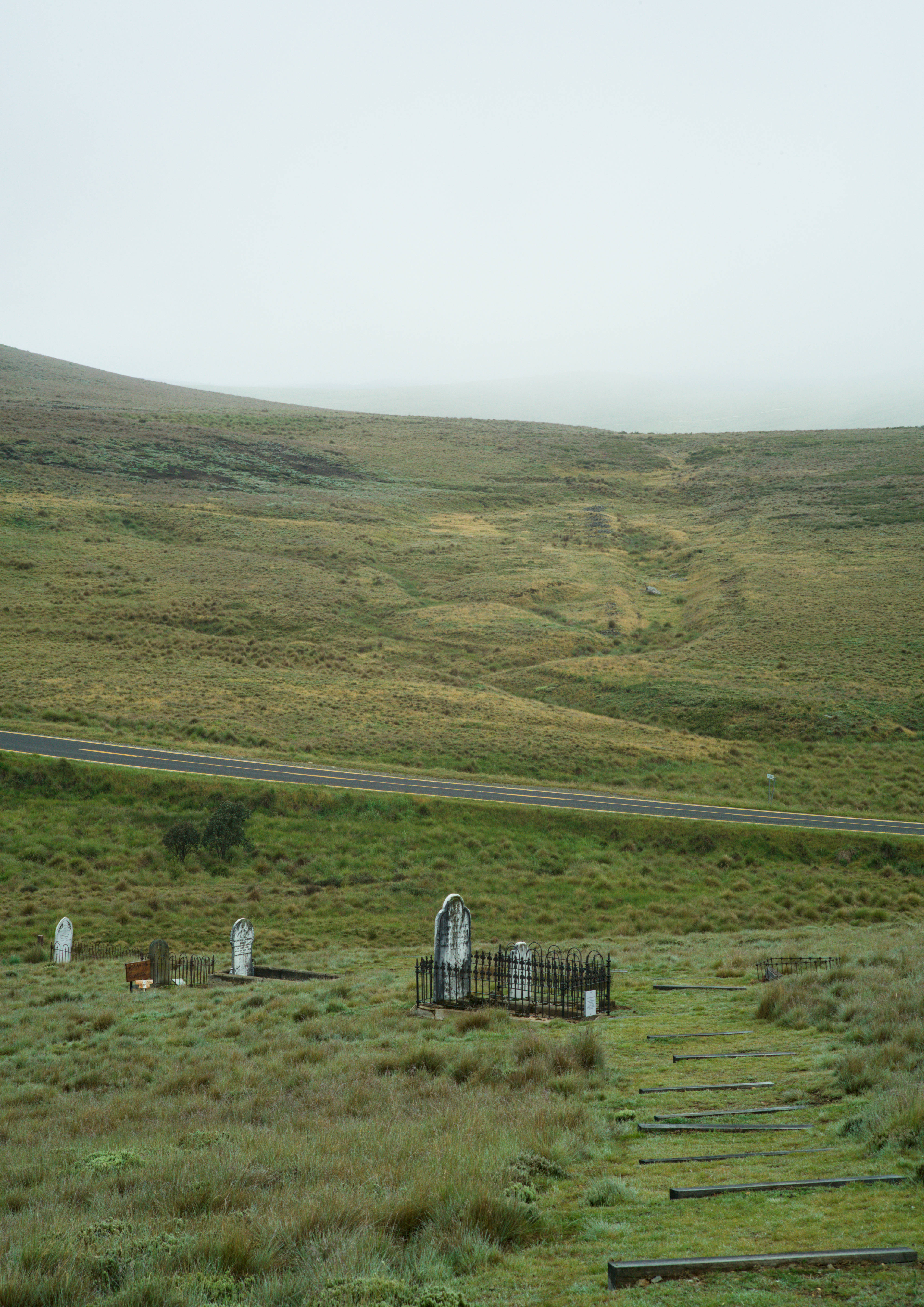 Remains, 1: Three tiers of burial plots on a hillside, separated from the upper slope by empty highway.