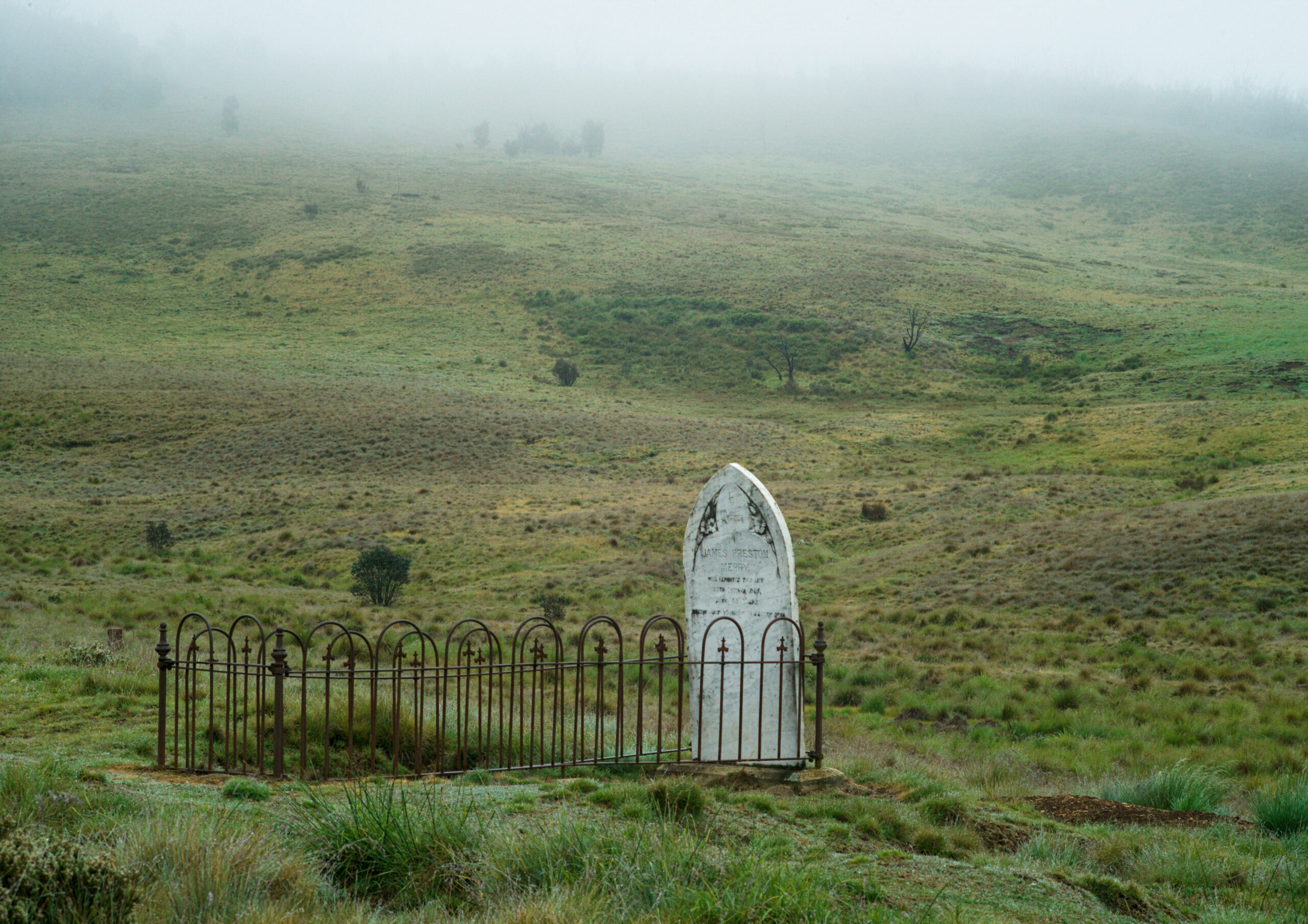 Remains, 7: A single fenced grave with white headstone.
